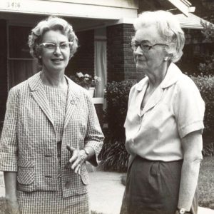 Pair of older white women with glasses standing outside house with covered porch