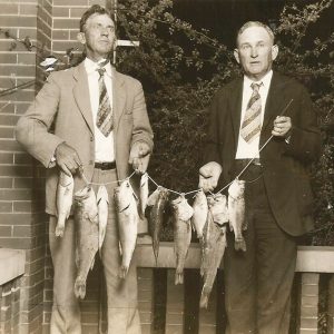 Two white men in suits with fish on a line