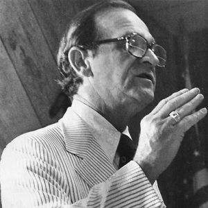 Old white man with glasses in striped suit speaking in public