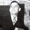 White man in suit and tie playing an accordion