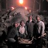 Three white men and one white woman with wheelbarrow filled with kindling and kiln behind them