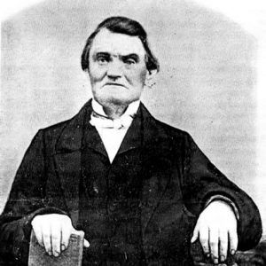 White man in suit sitting with book on his lap