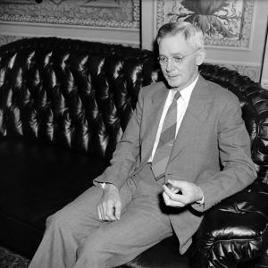 White man in glasses and suit sitting on a leather couch