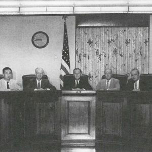 White men smiling from behind long desk with chairs