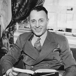 White man in suit sitting and smiling with open book in his lap