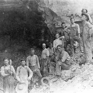 Group of white miners with tools before quarried side of a hill