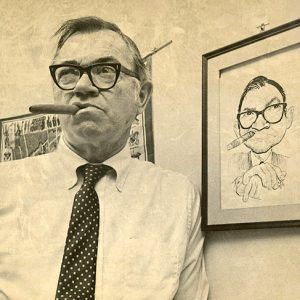 Older white man with glasses smoking a cigar before a caricature of the same