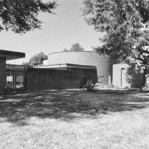 Single-story brick building with round section on grass with trees