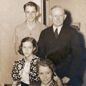 Portrait of white family with son and father standing behind seated girl who has her arm around seated mother