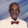 African-American man with mustache smiling in white suit with red bow tie