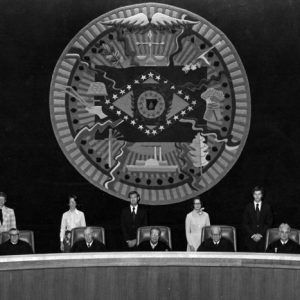 five judges in black robes at the bench with their clerks behind them under State Seal