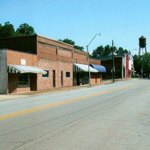 Brick storefronts on two-lane street with water tower in the background