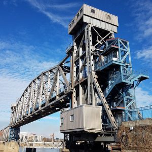 Close-up of steel arch walking bridge over river with elevator and stairs