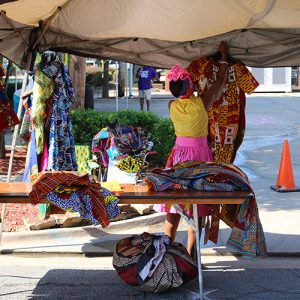 African-American woman hanging up multicolored clothing in a tent with table