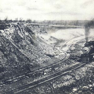 Steam locomotive with cars on tracks spewing smoke into the air