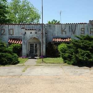 Spanish style concrete building with flagpole and parking lot