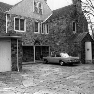 Multistory brick house with covered back entrance and single car garage with car on stone driveway