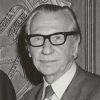 Old white man with glasses smiling in suit and tie