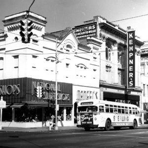 City street corner with tall store buildings and a city bus with ads on it