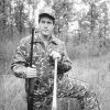 White man wearing camouflage and holding baseball bat and shotgun