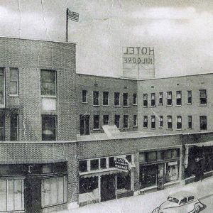 Three-story brick building on street with sign and flag on its roof