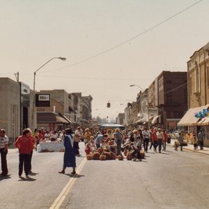 Mixed crowd on town street with multistory brick buildings on both sides of them