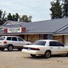 Single-story brick building with "King of Clubs private club" sign on gravel parking lot with parked cars