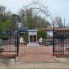 Stone monument with plaque and chairs with planters and trees on bricks behind iron gate with "Paul W. Klipsch Memorial Gardens" written in the iron