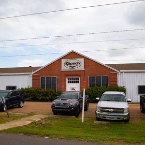 Parked cars outside single-story "Klipsch" building