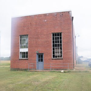 Red brick building with tall windows and blue side door with light above it and railing on walking path leading to it