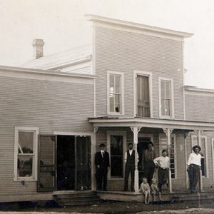 Group of white men woman and children outside two-story building