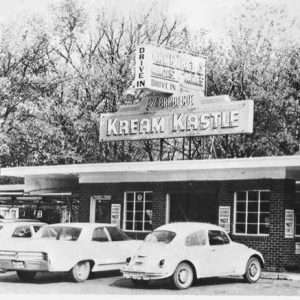 Cars parked outside single-story restaurant with neon sign