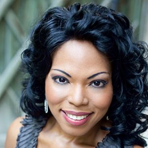 African-American woman with long curly hair smiling in sleeveless dress