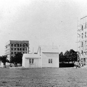 Five-story buildings under construction and single-story building with trees on grass