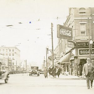 Cars on city street with tall buildings and signs and people walking