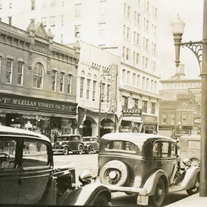 City street with storefronts and tall buildings and orate lamppost with parked cars