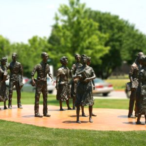 Group of nine bronze sculptures depicting male and female high school students carrying books on concrete pad on lawn