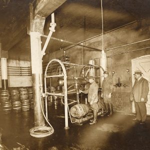 Three white men in brewery with barrels and machinery