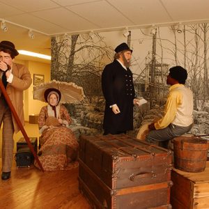 Museum display with mannequins in period costume as a white surveyor, woman with parasol, steamboat captain, and black man