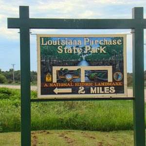 Wooden sign for "Louisiana State Park" in grass next to highway