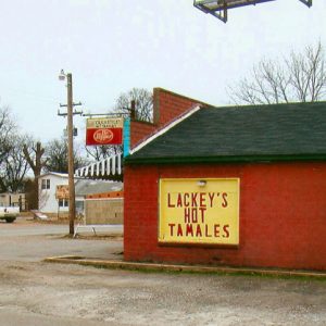 Side view of single-story brick building on town street corner with "Lackey's Hot Tamales" sign on its side