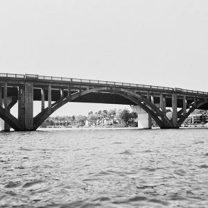 Concrete arch bridge over lake with houses in the background