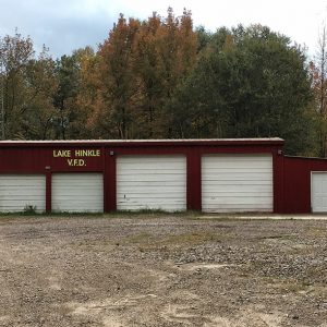 Red building with four garage bay doors and front door on gravel