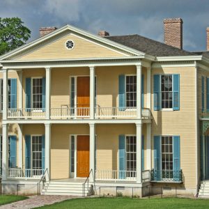 yellow two-story house with covered porch and balcony and light blue stutters