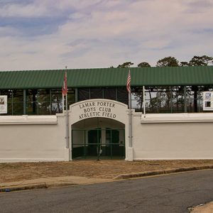 Entrance gate to athletic field with green metal roof and paved road in foreground