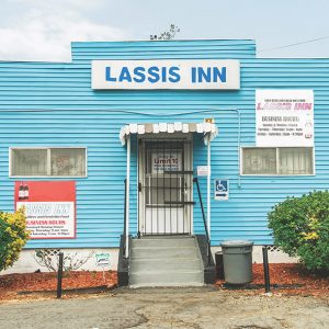 Single-story building with signs blue siding and awning over the entrance