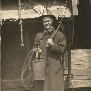 White man in uniform with firemen's hat bucket and hatchet on set