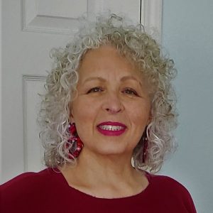 African American woman with long curly gray hair smiling in red shirt and earrings