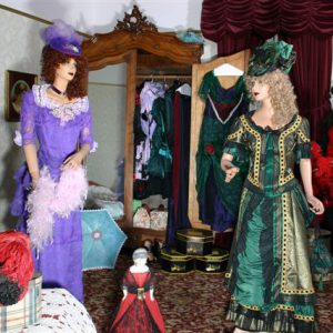 Two mannequins wearing fancy dresses in room with fashion artifacts