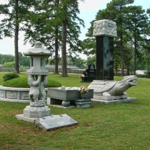 Asian-inspired grave markers in cemetery with green grass and tall trees